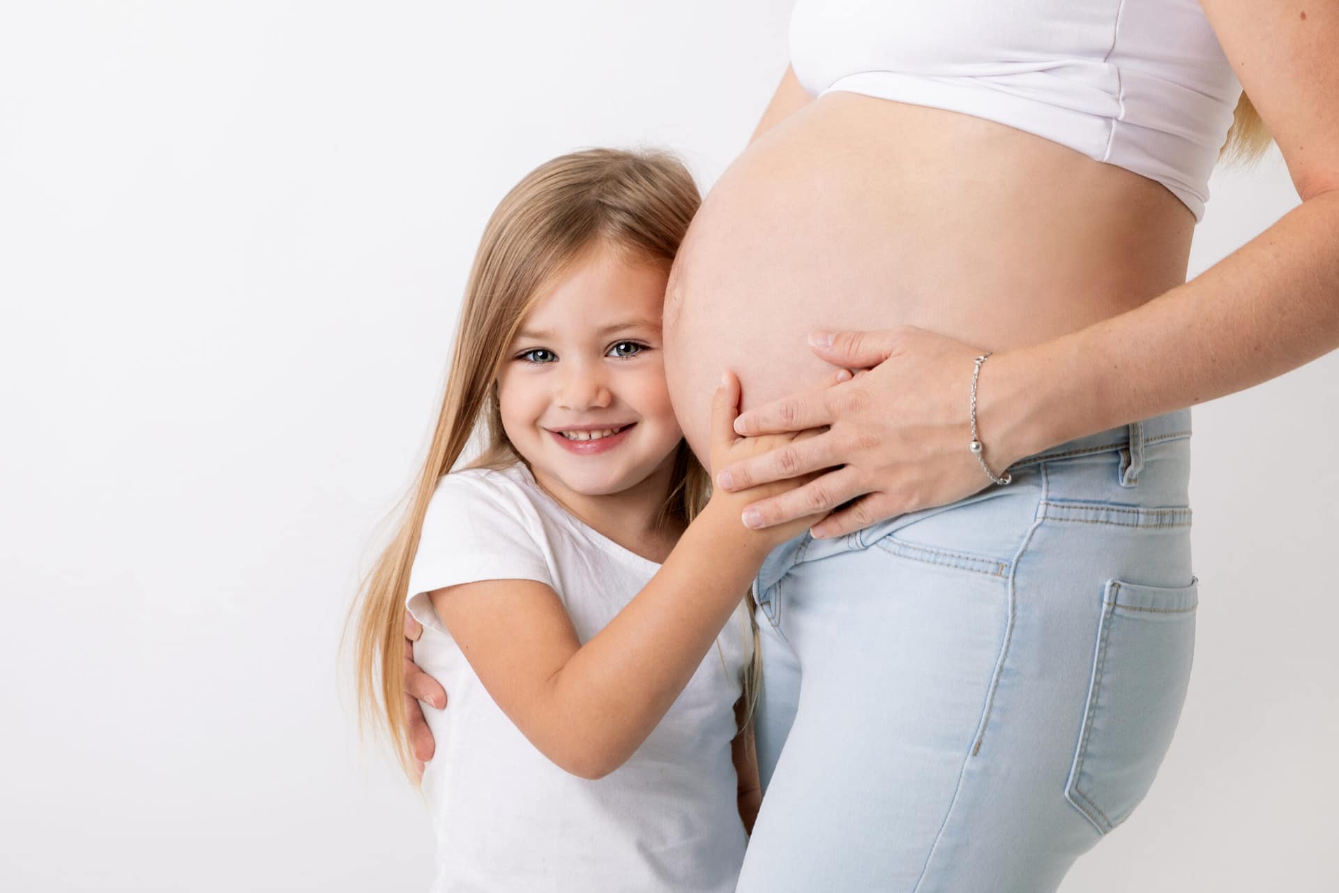 teliérové těhotenské focení Praha: Něžný detailní portrét těhotné ženy cradling odhalené bříško oběma rukama.